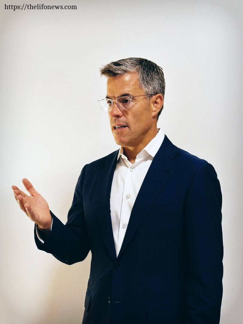 Brook Taube, a man in a suit and glasses, is speaking, showcasing a formal and authoritative demeanor.